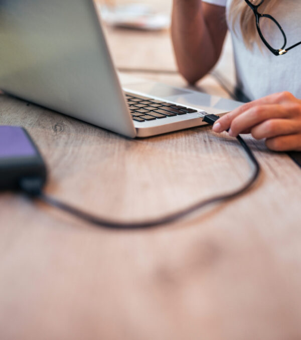 Close-up image of a woman freelancer connecting an external hard drive to the laptop.